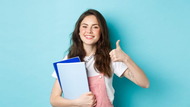 young-woman-attend-courses-girl-student-studying-holding-notebooks-showing-thumb-up-approval-recommending-company-standing-blue-background-scaled-2.jpg